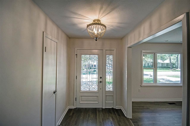 foyer entrance with a textured ceiling, dark hardwood / wood-style flooring, plenty of natural light, and an inviting chandelier