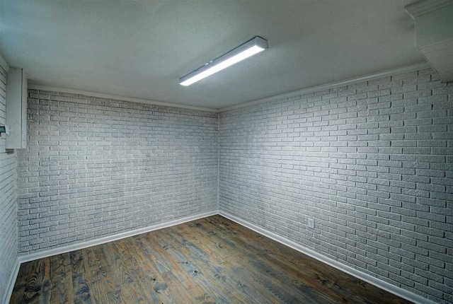 unfurnished room with brick wall, ornamental molding, and dark hardwood / wood-style floors