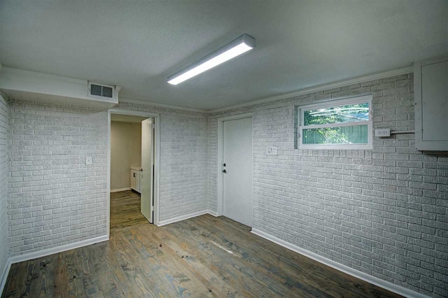 empty room featuring brick wall, crown molding, and wood-type flooring