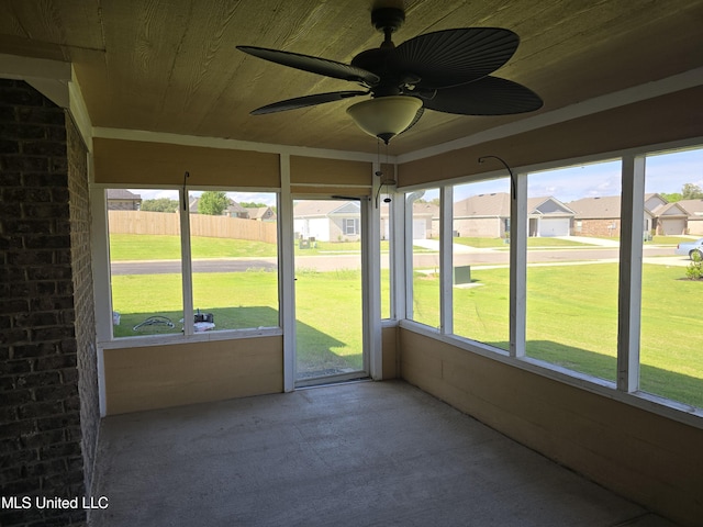 unfurnished sunroom featuring a healthy amount of sunlight, a residential view, and a ceiling fan