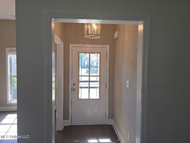 doorway with an inviting chandelier, baseboards, and wood finished floors