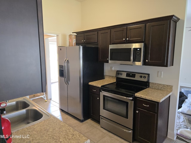 kitchen featuring dark brown cabinetry, a sink, light countertops, light tile patterned floors, and stainless steel appliances