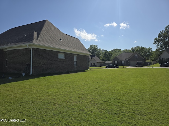 view of side of home featuring roof with shingles, a yard, and brick siding