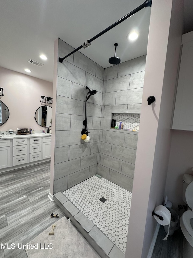 bathroom with double vanity, a tile shower, and wood finished floors