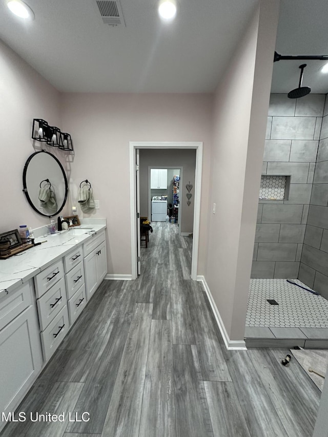 bathroom with tiled shower, visible vents, and wood finished floors