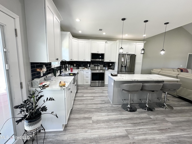 kitchen featuring white cabinetry, stainless steel appliances, backsplash, a kitchen island, and a breakfast bar area