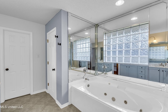 full bath with a sink, a textured ceiling, a tub with jets, tile patterned flooring, and baseboards