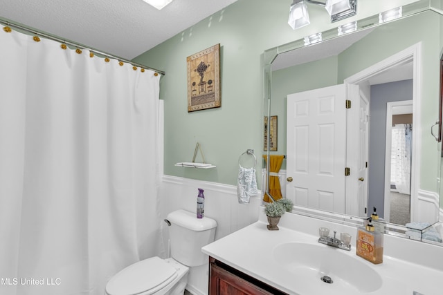 full bath featuring a shower with curtain, toilet, a textured ceiling, wainscoting, and vanity