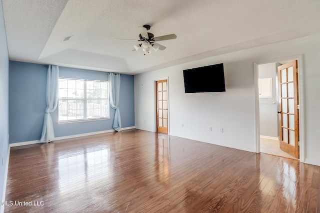 unfurnished room featuring baseboards, a textured ceiling, a tray ceiling, and wood finished floors