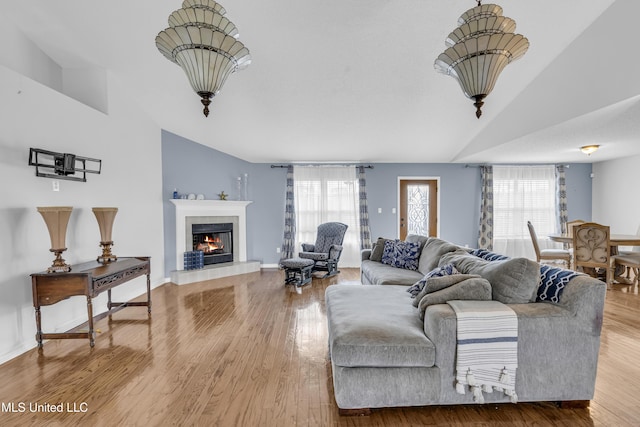 living room featuring baseboards, wood finished floors, a tile fireplace, and vaulted ceiling