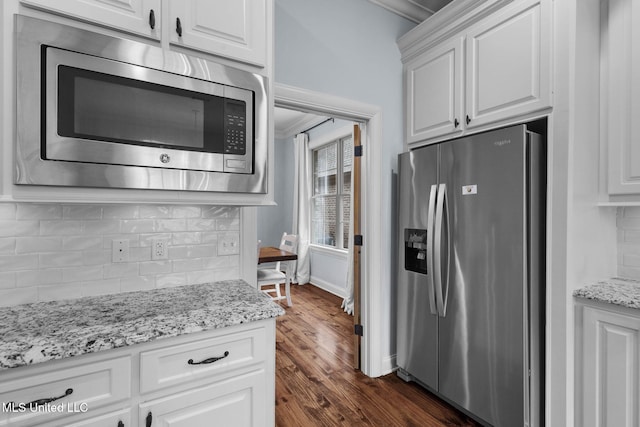 kitchen featuring appliances with stainless steel finishes, white cabinetry, dark hardwood / wood-style flooring, decorative backsplash, and light stone countertops