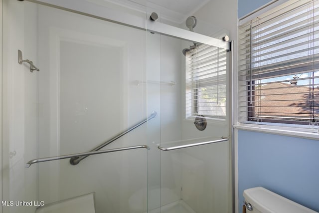 bathroom with toilet, ornamental molding, and a shower with shower door