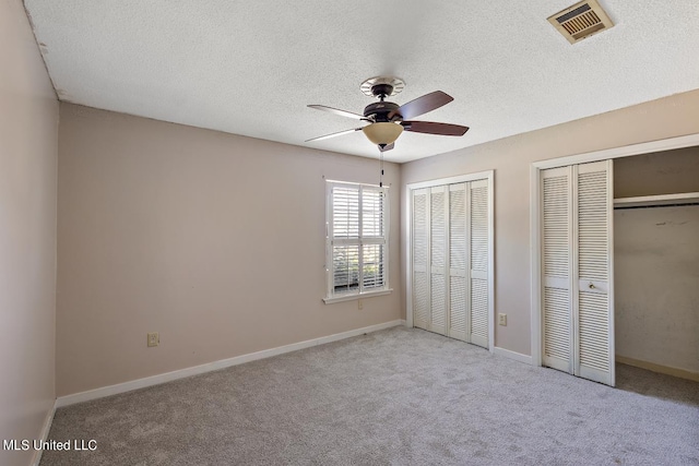 unfurnished bedroom featuring light carpet, a textured ceiling, two closets, and ceiling fan