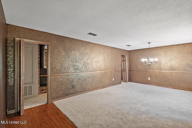 empty room featuring a notable chandelier, hardwood / wood-style floors, and a textured ceiling