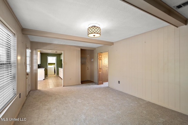 empty room with light carpet, beamed ceiling, a textured ceiling, and plenty of natural light