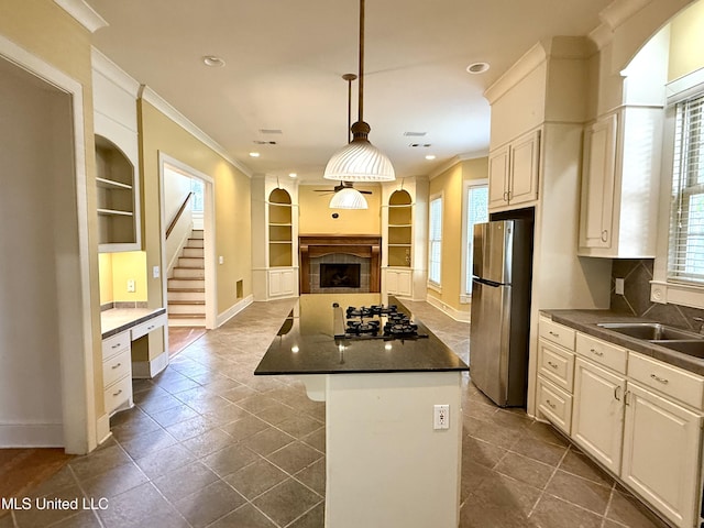 kitchen featuring built in shelves, gas stovetop, ornamental molding, freestanding refrigerator, and dark countertops