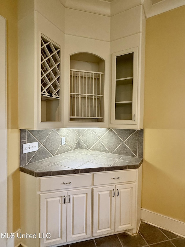 interior space with backsplash, glass insert cabinets, white cabinetry, dark tile patterned flooring, and baseboards