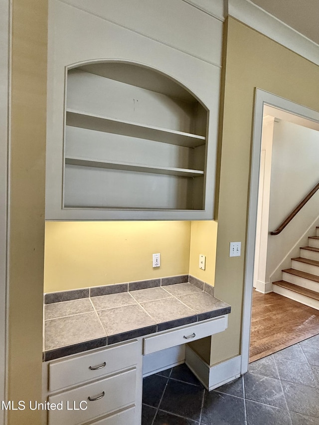 unfurnished office with baseboards, built in desk, and dark tile patterned flooring