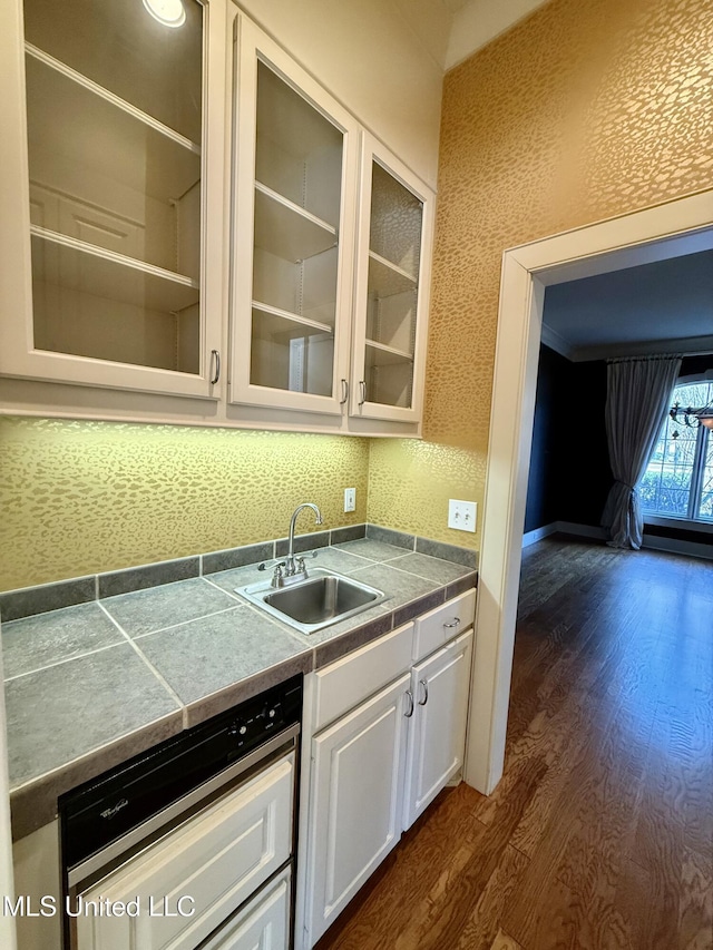 kitchen with dishwashing machine, dark wood-type flooring, a sink, white cabinets, and glass insert cabinets