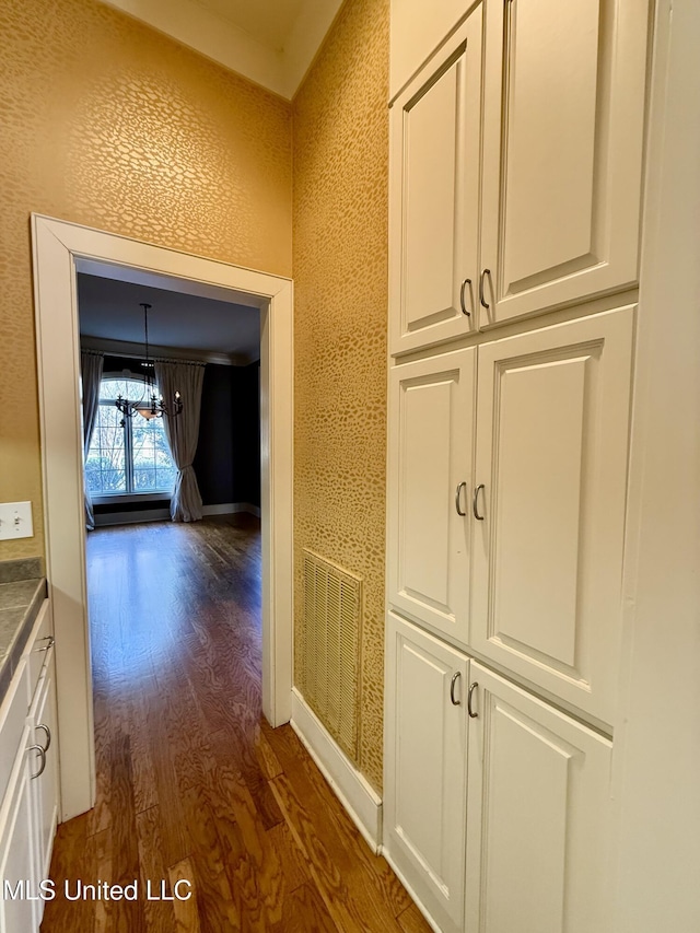 hall featuring an inviting chandelier, visible vents, baseboards, and dark wood-type flooring