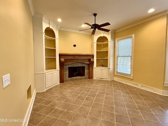 unfurnished living room featuring a ceiling fan, built in shelves, crown molding, and a tiled fireplace