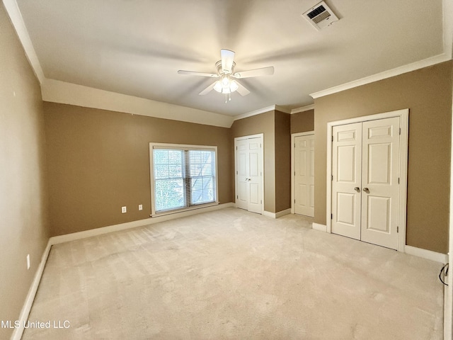 unfurnished bedroom with baseboards, light colored carpet, two closets, and ornamental molding