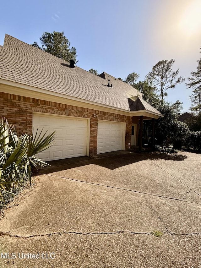 view of side of home with driveway, an attached garage, roof with shingles, and brick siding