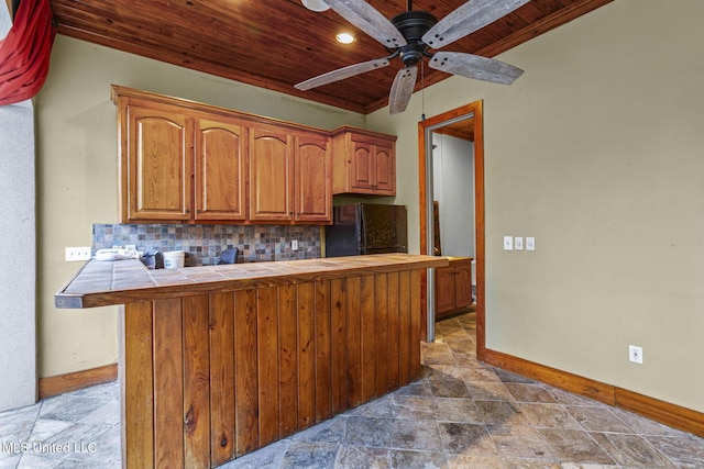 kitchen featuring tile countertops, decorative backsplash, freestanding refrigerator, wood ceiling, and stone finish floor