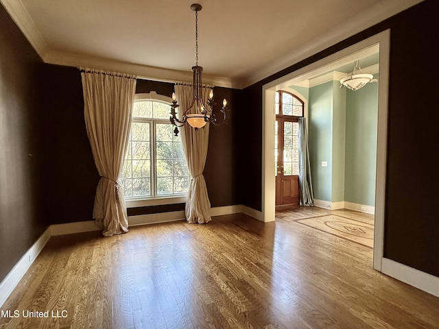 unfurnished dining area featuring baseboards, crown molding, an inviting chandelier, and wood finished floors