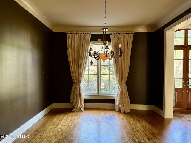 unfurnished dining area with ornamental molding, wood finished floors, a wealth of natural light, and a notable chandelier