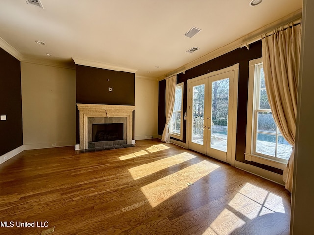 unfurnished living room with wood finished floors, visible vents, baseboards, french doors, and crown molding