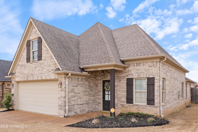 french country style house featuring a garage, a shingled roof, concrete driveway, and brick siding