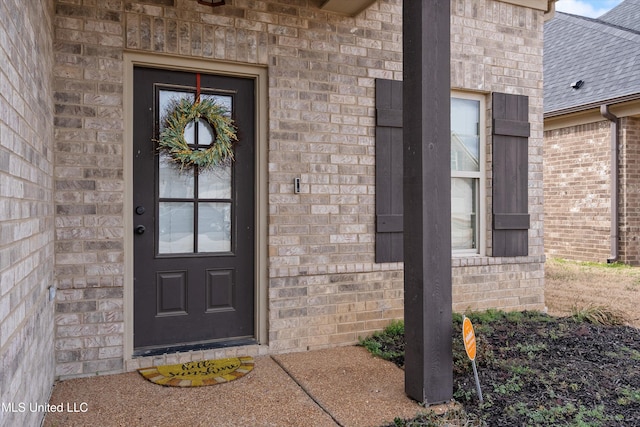 property entrance with a shingled roof and brick siding