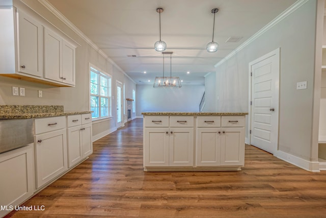 kitchen with hardwood / wood-style flooring, ornamental molding, pendant lighting, white cabinets, and light stone counters