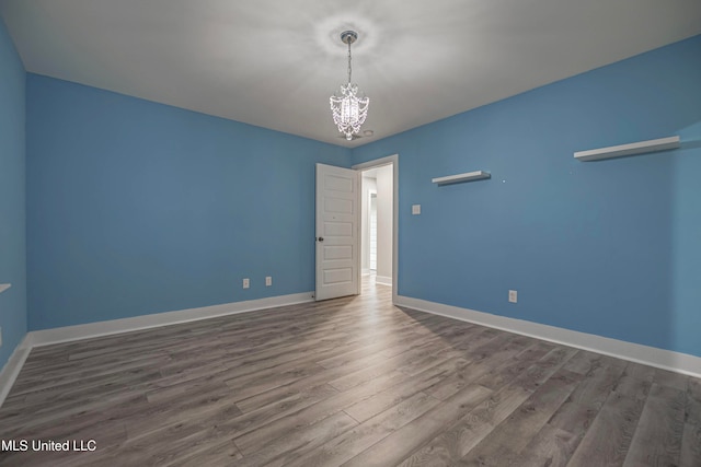 spare room with hardwood / wood-style flooring and an inviting chandelier