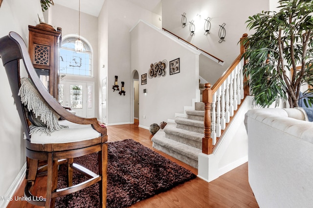foyer with a chandelier, a towering ceiling, stairway, baseboards, and wood finished floors