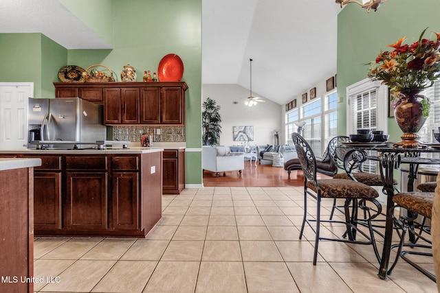 kitchen featuring stainless steel fridge with ice dispenser, light tile patterned flooring, light countertops, decorative backsplash, and high vaulted ceiling