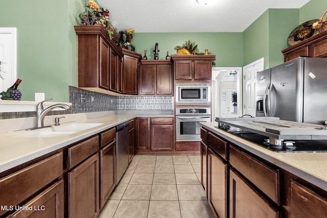 kitchen with appliances with stainless steel finishes, a sink, light countertops, decorative backsplash, and a textured ceiling