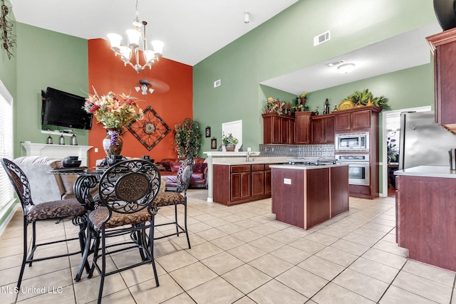 kitchen with appliances with stainless steel finishes, high vaulted ceiling, a chandelier, light tile patterned floors, and light countertops