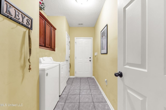 washroom featuring washing machine and clothes dryer, cabinet space, a textured ceiling, light tile patterned floors, and baseboards