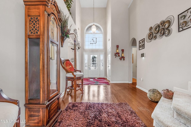 entryway featuring a towering ceiling, arched walkways, wood finished floors, baseboards, and a chandelier