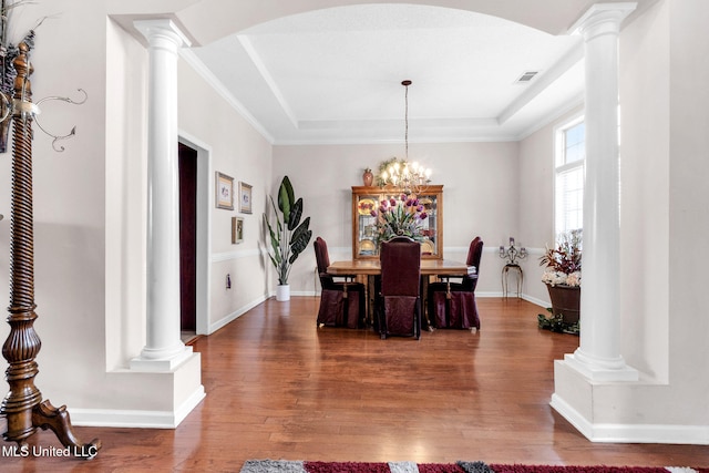 dining area with decorative columns, wood finished floors, a tray ceiling, arched walkways, and baseboards