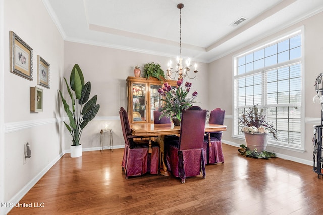 dining area with a chandelier, plenty of natural light, wood finished floors, a tray ceiling, and crown molding