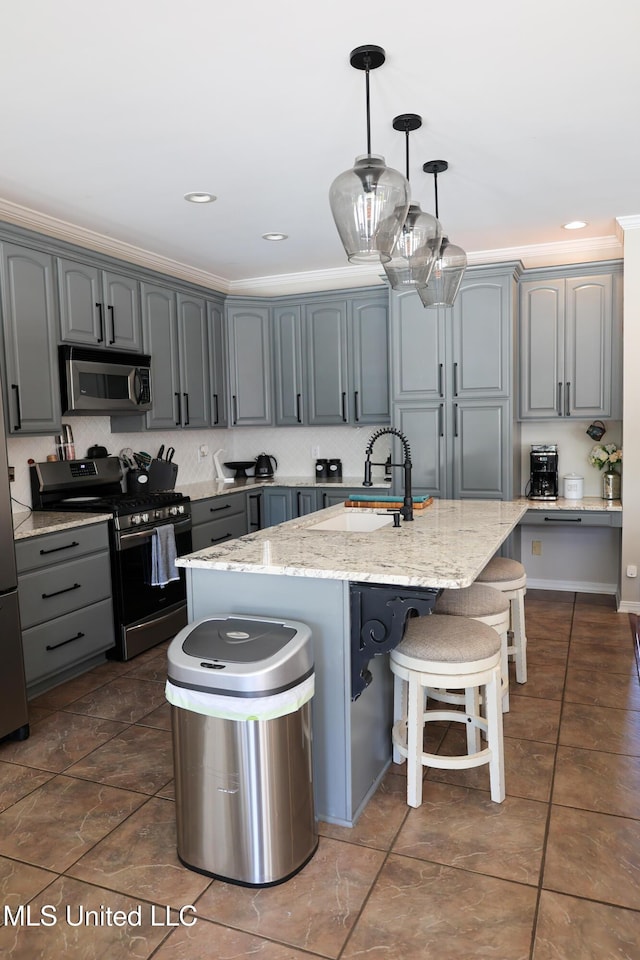 kitchen featuring light stone countertops, appliances with stainless steel finishes, ornamental molding, gray cabinetry, and an island with sink