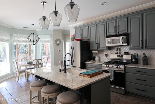 kitchen with pendant lighting, crown molding, an island with sink, appliances with stainless steel finishes, and light stone counters