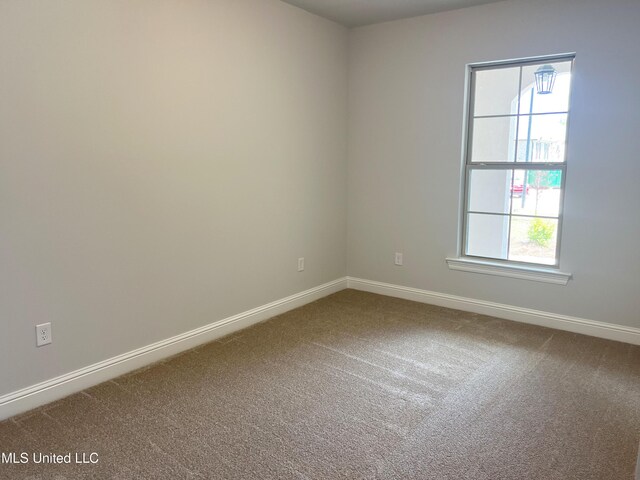 spare room featuring dark colored carpet and baseboards