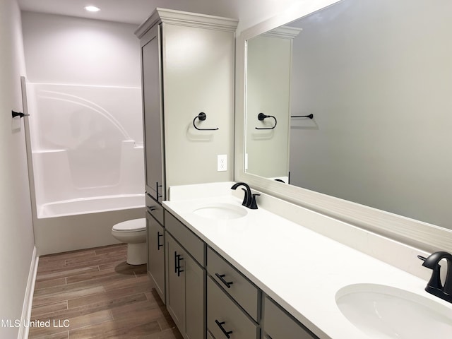 full bath with toilet, double vanity, a sink, and wood finished floors