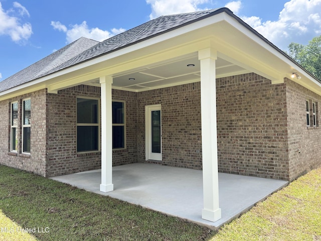 back of house with a shingled roof, a patio area, and brick siding