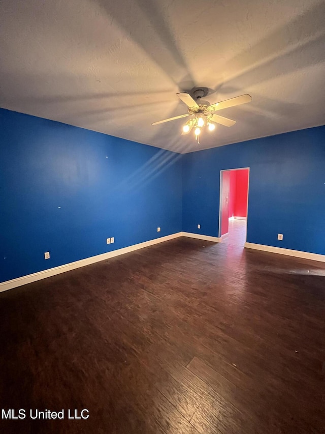 empty room featuring a ceiling fan, a textured ceiling, baseboards, and dark wood-type flooring