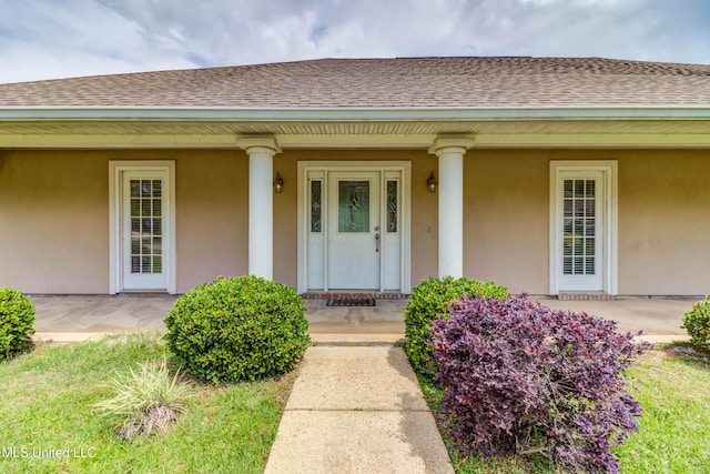 entrance to property featuring a porch, stucco siding, and roof with shingles